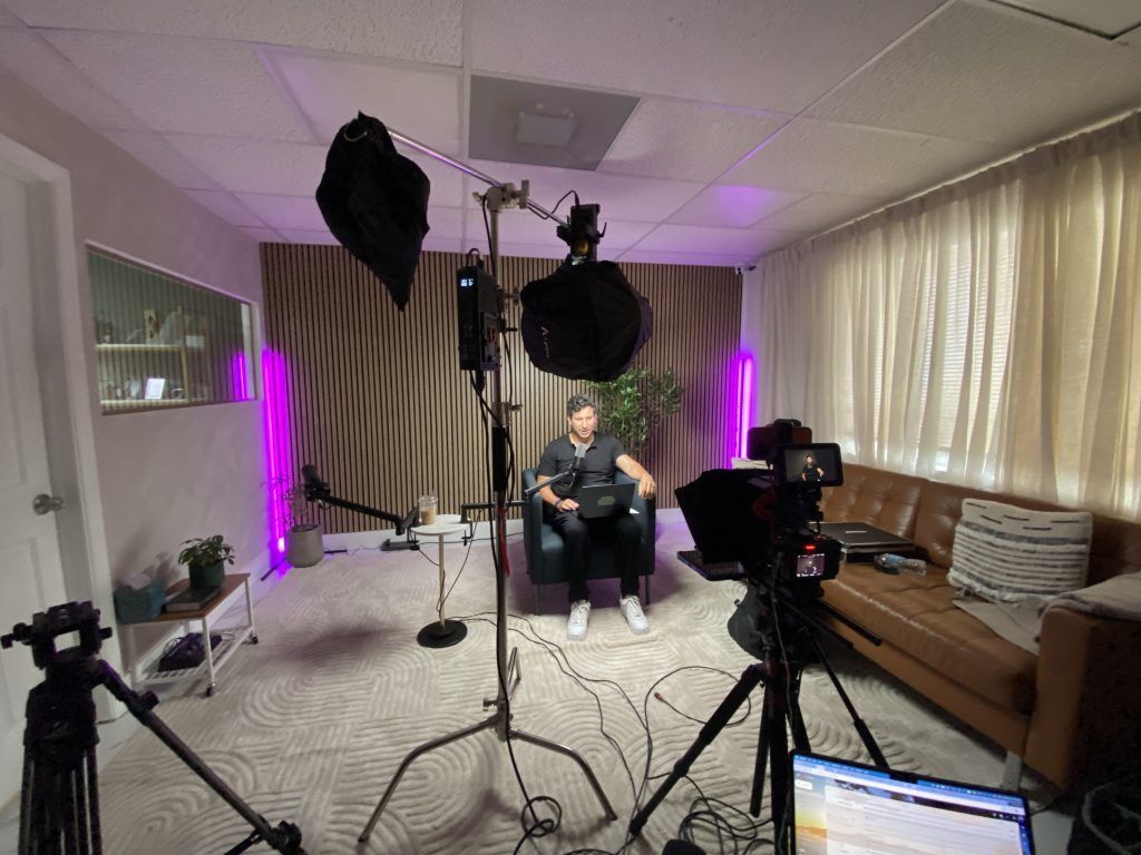 Wide view of the podcast studio during a shoot, with two lights, cameras and a host seated on set