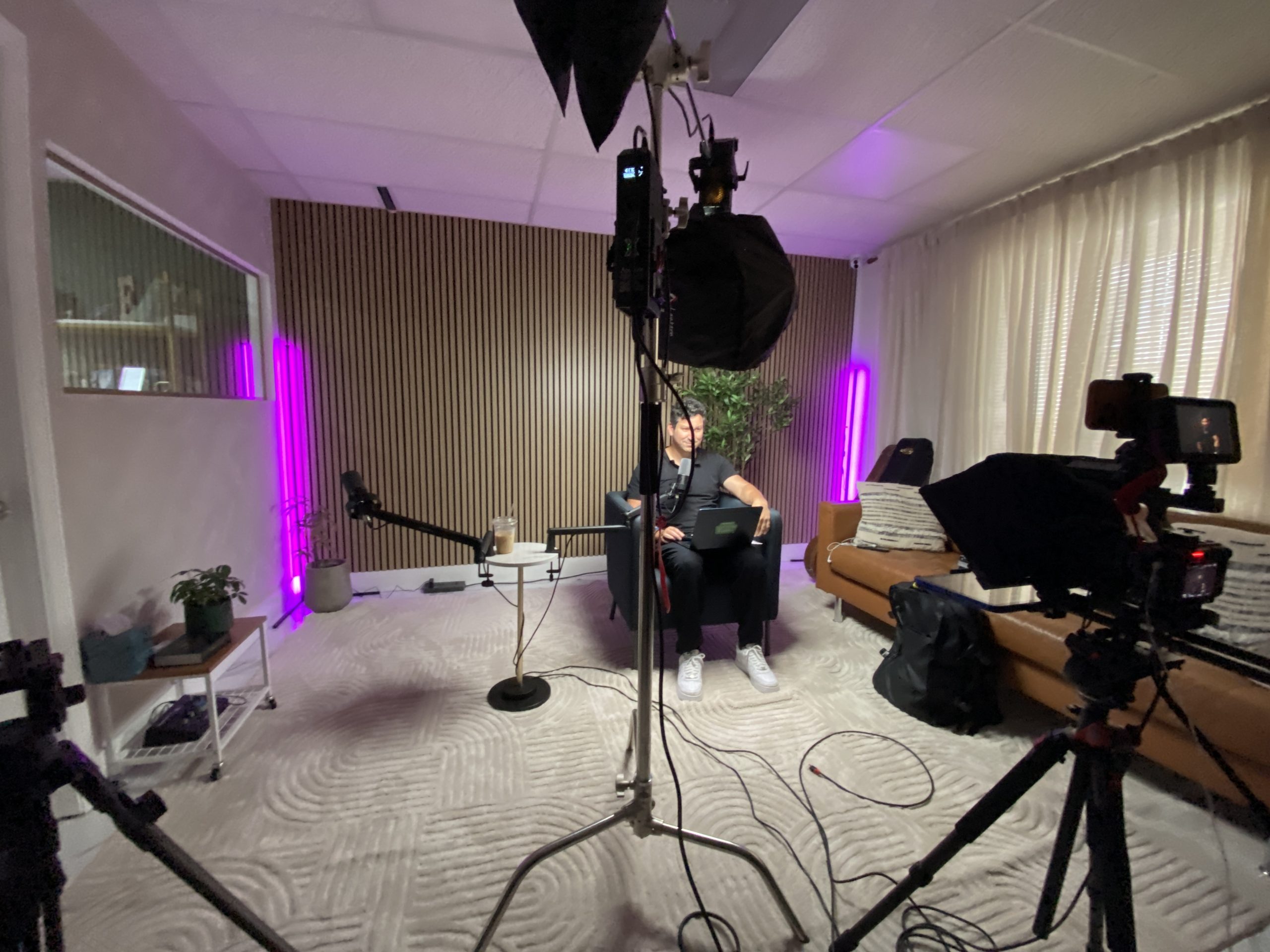 Wide view of the Spark Studio podcast room with cameras, lighting stands and a guest seated in front of the wood slat wall