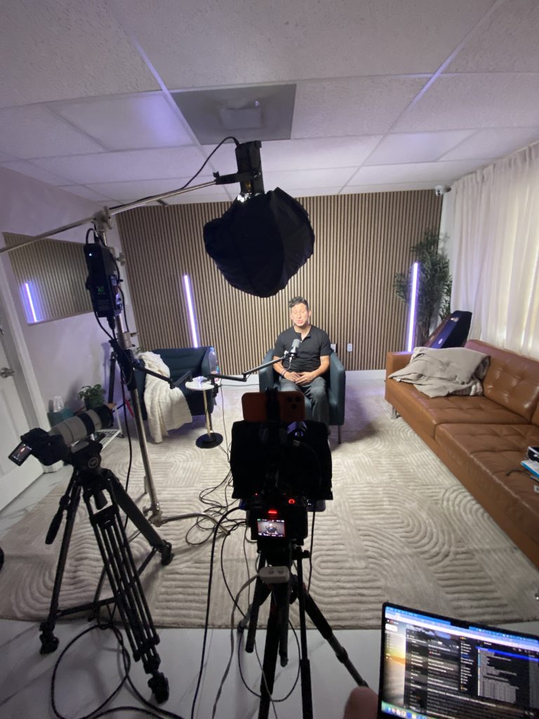 Two-camera podcast setup shot from behind the operator position, with the host seated facing the lenses