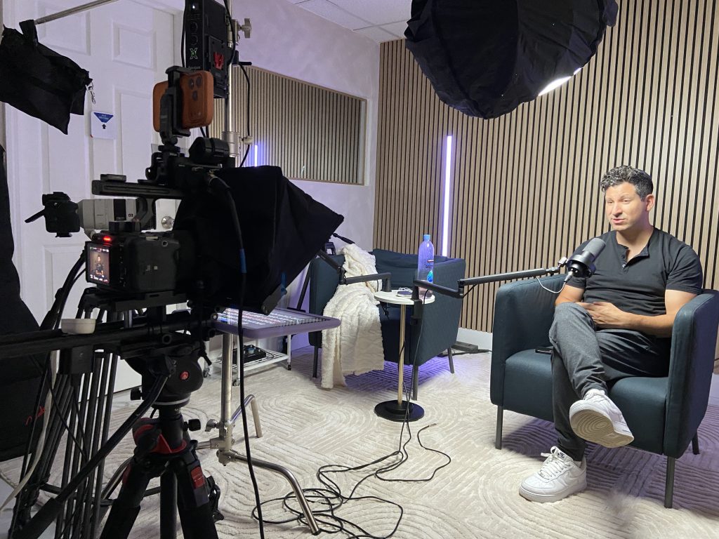 Camera monitor showing the framed shot while a podcast host talks into a boom microphone