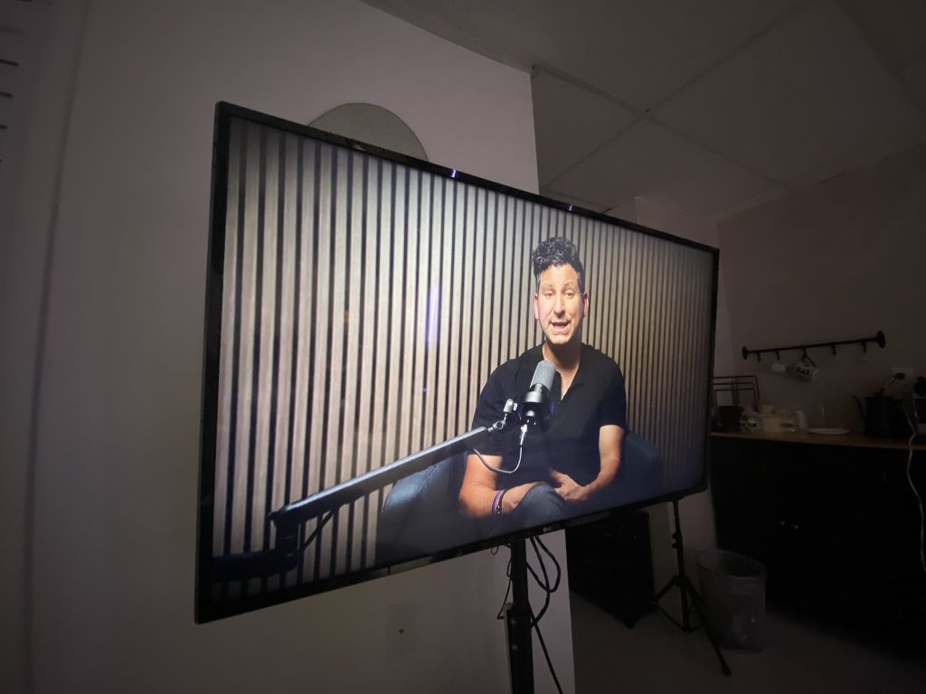 Studio monitor on a stand showing the live camera feed of a host recording a podcast episode