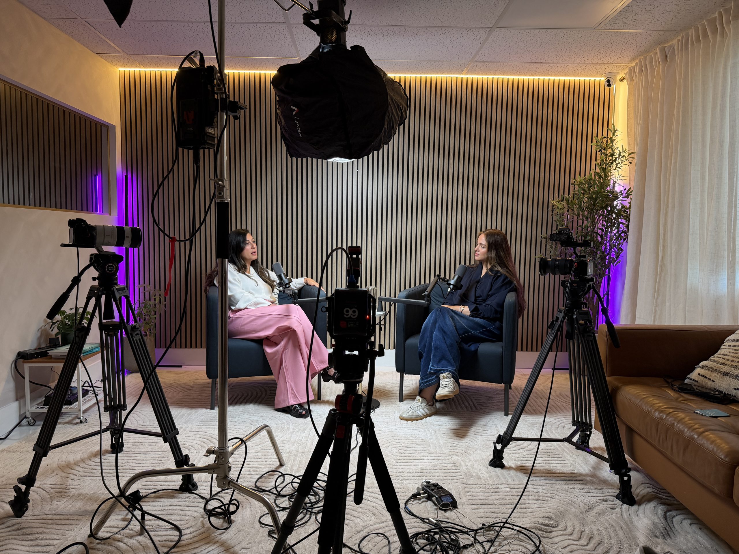 Wide view of the podcast studio with several cameras on tripods recording two people in conversation