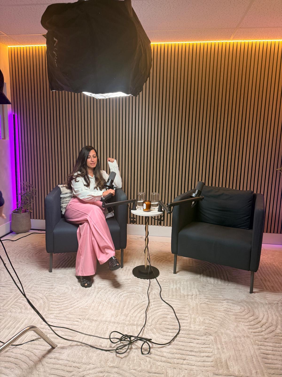 Woman seated in an armchair recording a podcast episode under warm and purple studio lighting