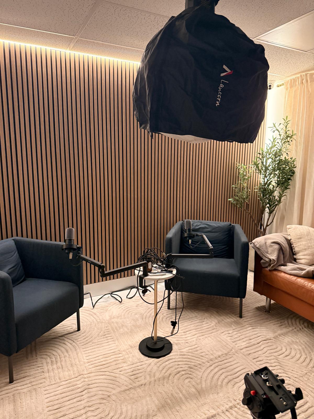 Grey armchairs and a brown leather sofa in the warmly lit podcast studio with wood slat walls