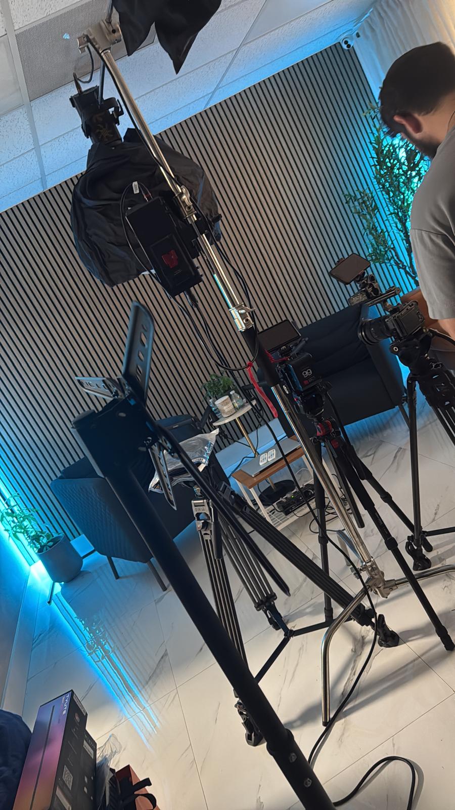 Video cameras on tripods facing the podcast set, lit with blue accent lighting