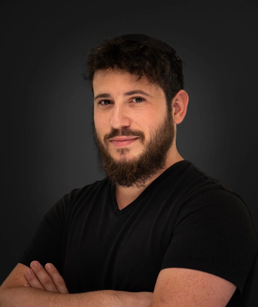 Dov Gurewicz, director of photography and producer at Spark Studio, arms folded against a dark background