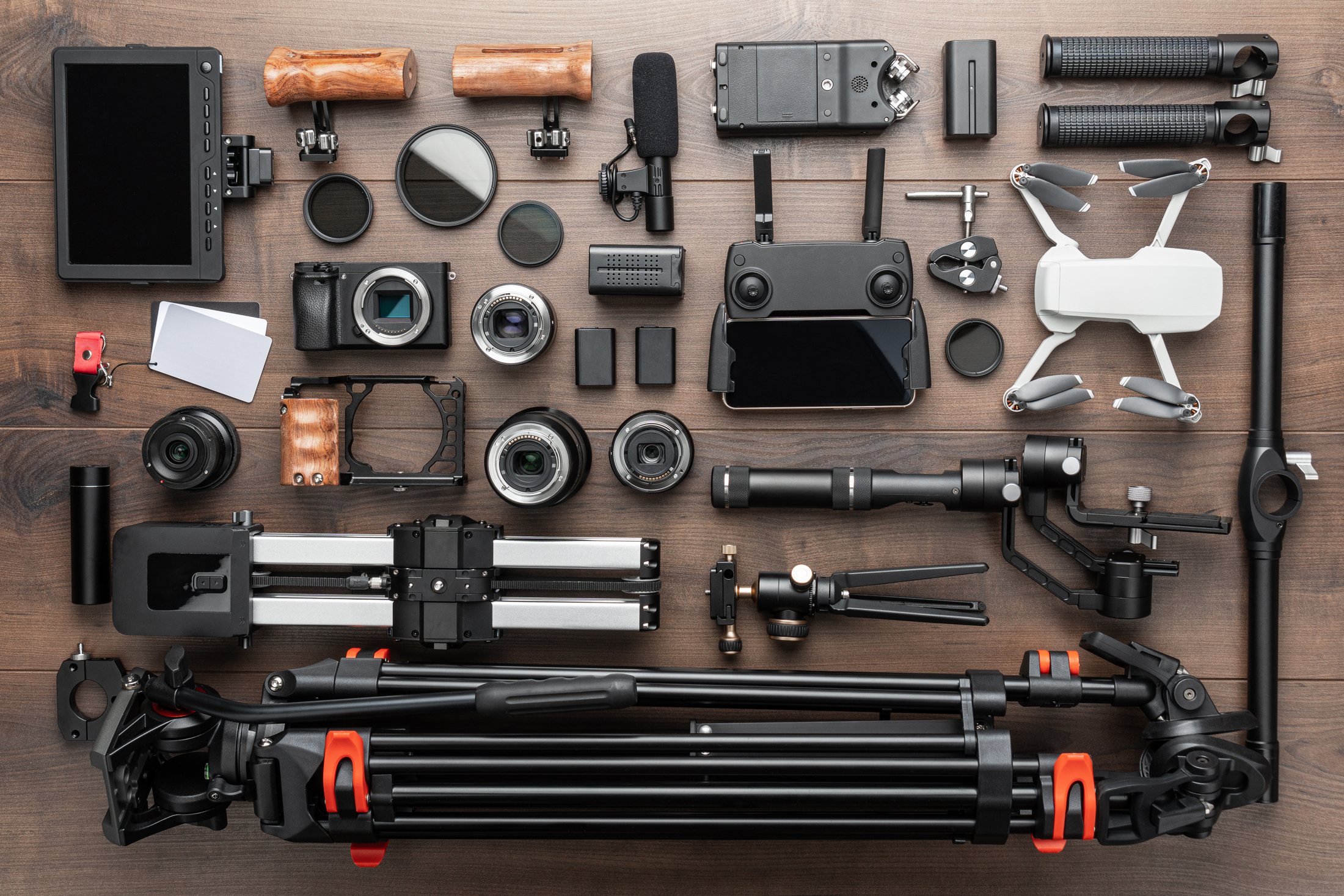 Video and photography equipment laid out flat: camera bodies, lenses, monitor, microphone and a tripod