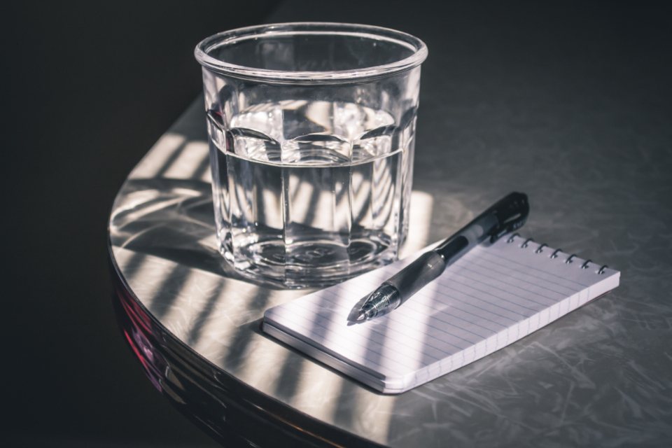 Notebook, pen and a glass of water on a dark desk